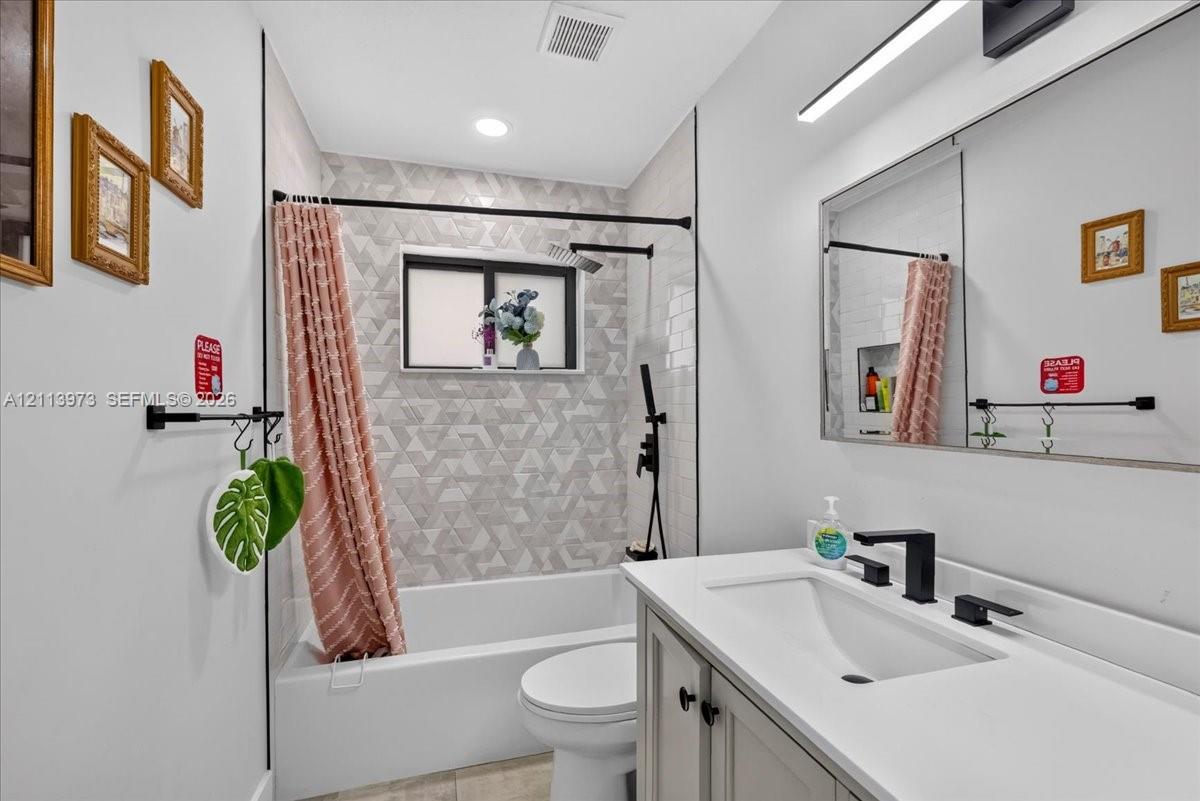 Bathroom featuring a vanity with a white countertop, matte black fixtures, a shower-tub combination with geometric tile surround, and a large wall-mounted mirror