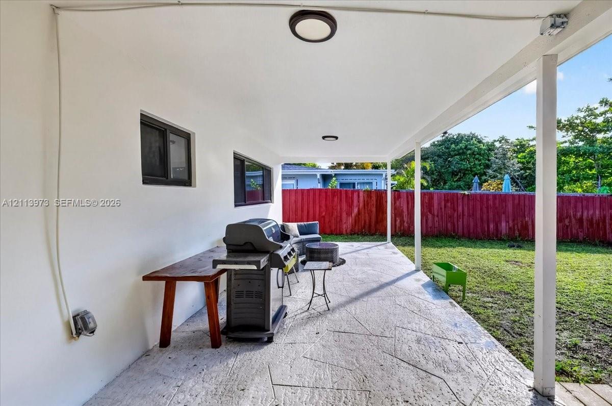 Covered patio featuring stamped concrete flooring, flush-mount ceiling lighting, and a red privacy fence bordering the rear yard