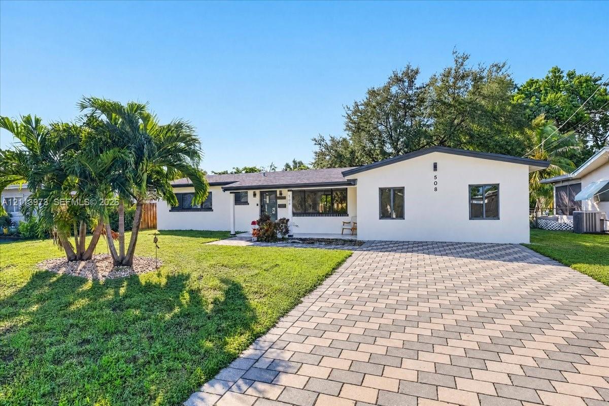 Single-story exterior featuring a light-toned smooth facade, concrete paver driveway, dark-framed windows, and a manicured front lawn with established palms Single-story exterior featuring a light-toned smooth facade, concrete paver driveway, dark-framed windows, and a manicured front lawn with established palms