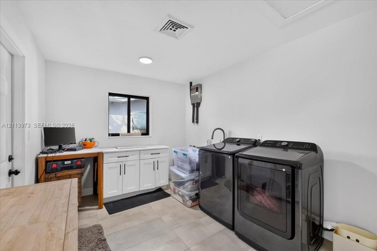 Laundry area featuring white shaker-style cabinetry, a rectangular window with a dark frame, and light-toned tile flooring