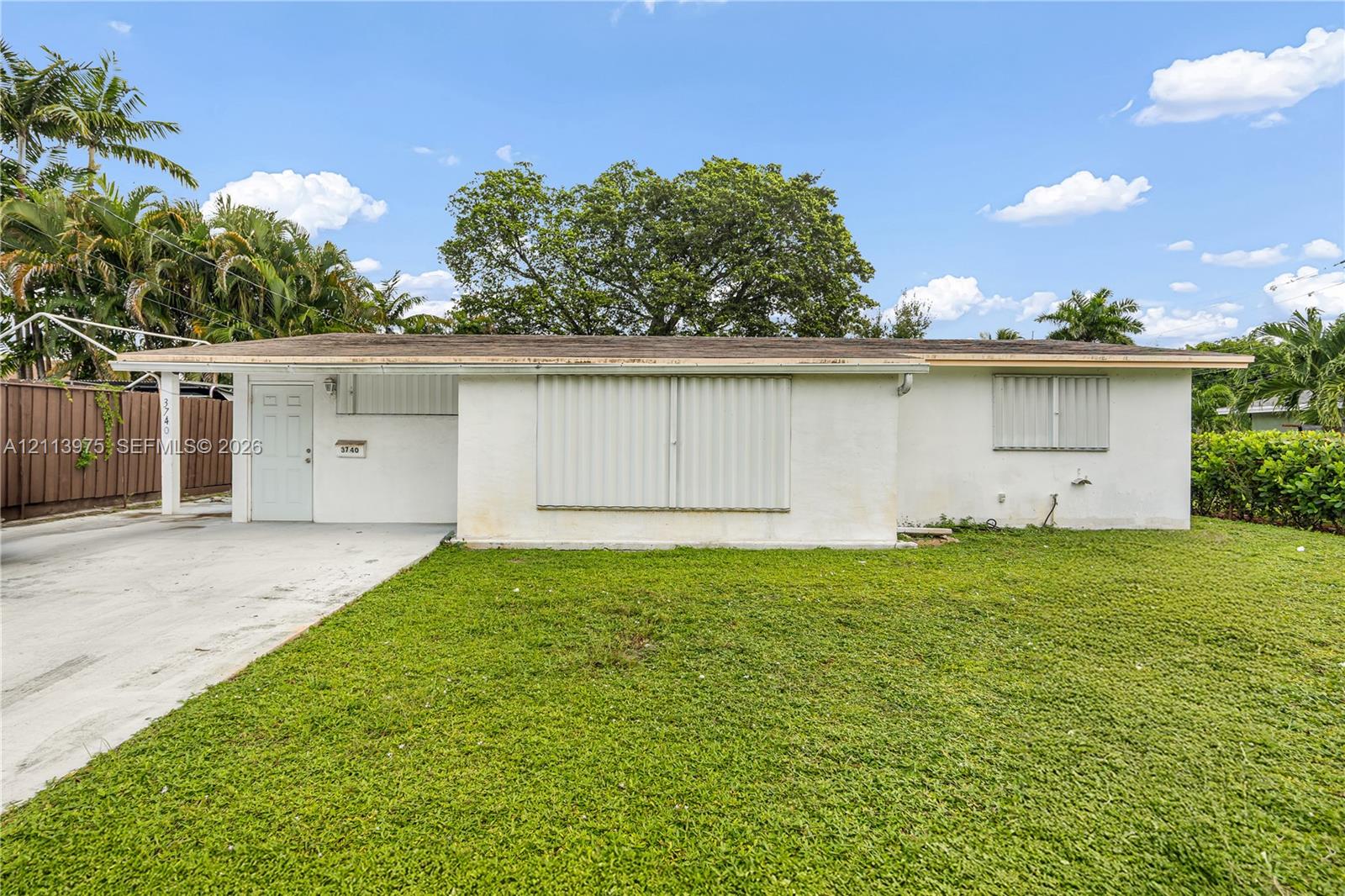 Single-story exterior featuring a light-toned facade, flat roofline, concrete driveway, and attached metal storm shutters