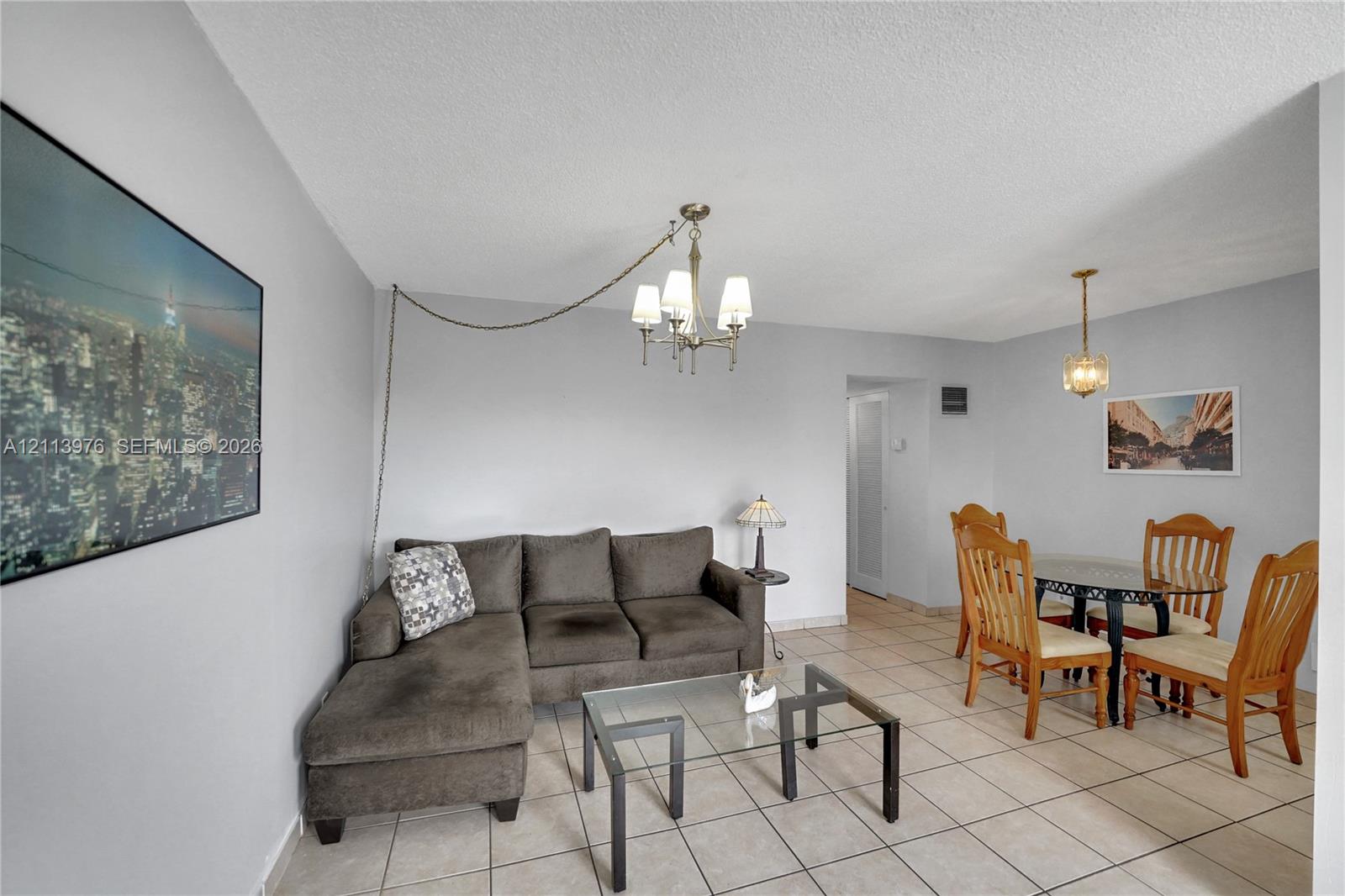 Living area featuring tile flooring, neutral wall paint, and two overhead multi-light chandeliers