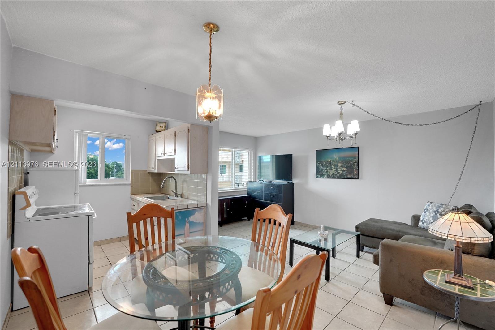 Open-concept interior featuring large-format tile flooring, dual hanging pendant light fixtures, and windows providing natural light