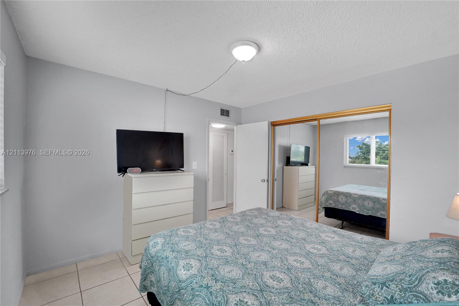 Neutral-toned bedroom featuring tile flooring, sliding mirror-panel closet doors, and a ceiling-mounted light fixture