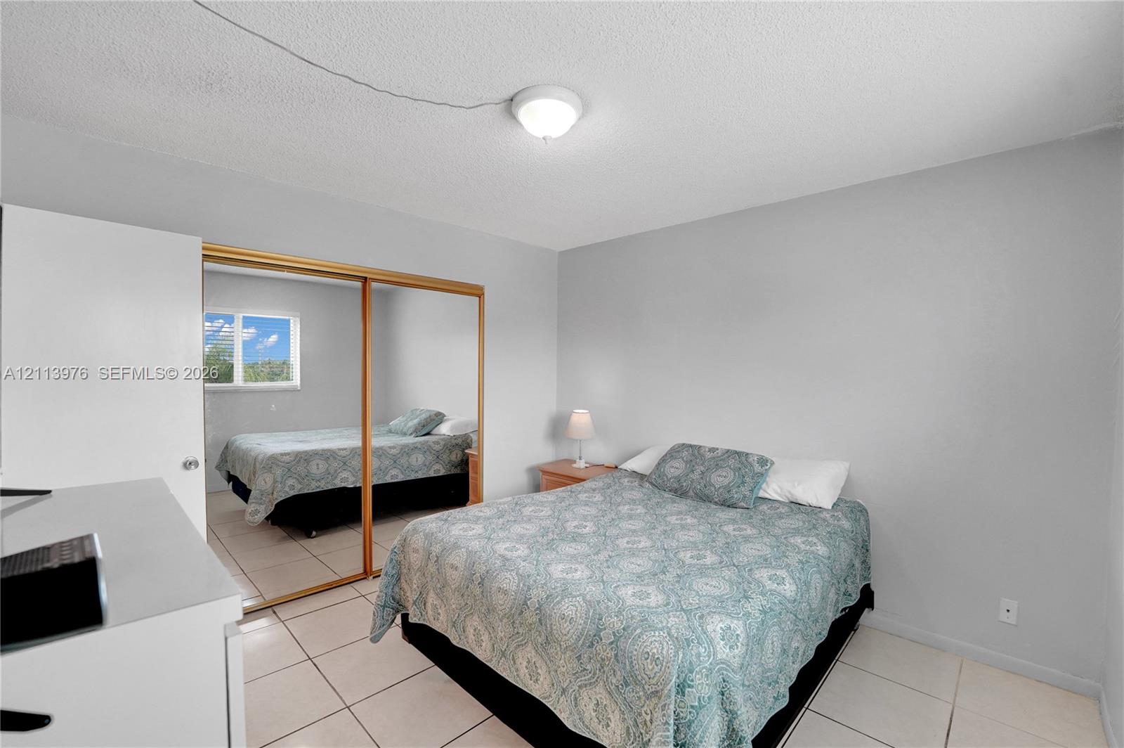 Bedroom featuring neutral wall paint, tile flooring, and a mirrored sliding closet door