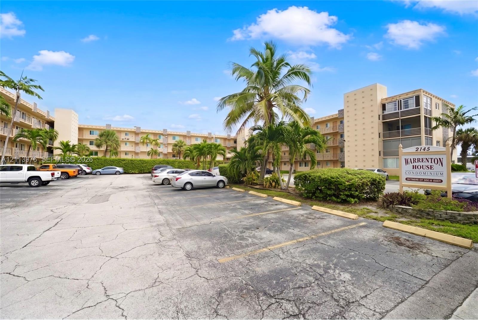 Multi-story residential complex featuring stucco exterior walls, private balconies, and mature palm tree landscaping