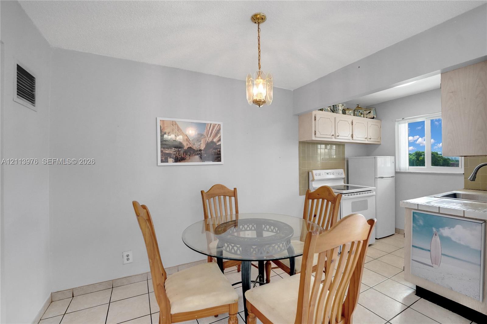 Kitchen area featuring tile flooring, ceiling-mounted decorative pendant lighting, upper cabinetry, and a window