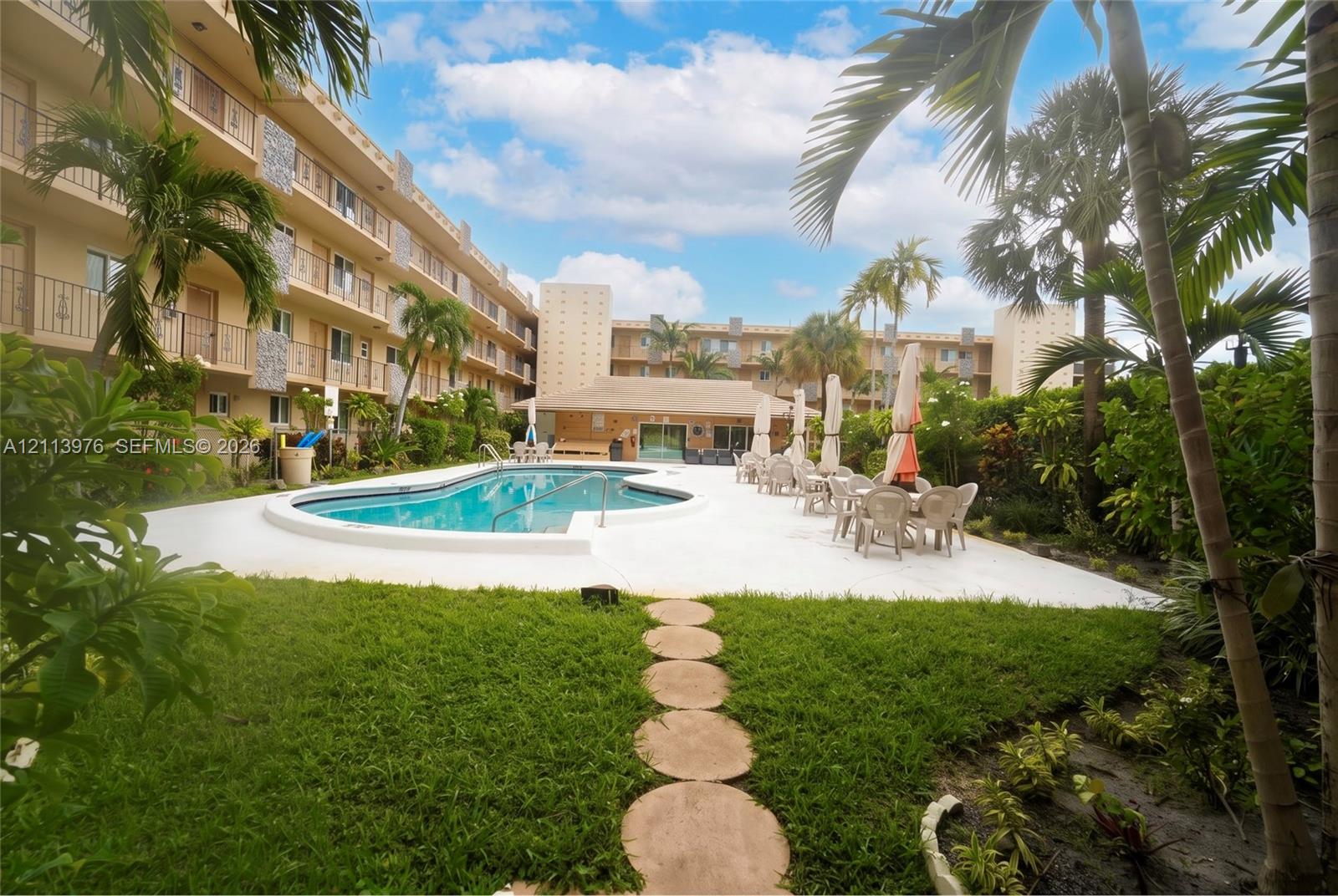 Swimming pool area featuring a concrete deck, stepping stone walkway, manicured lawn, and mature palm trees