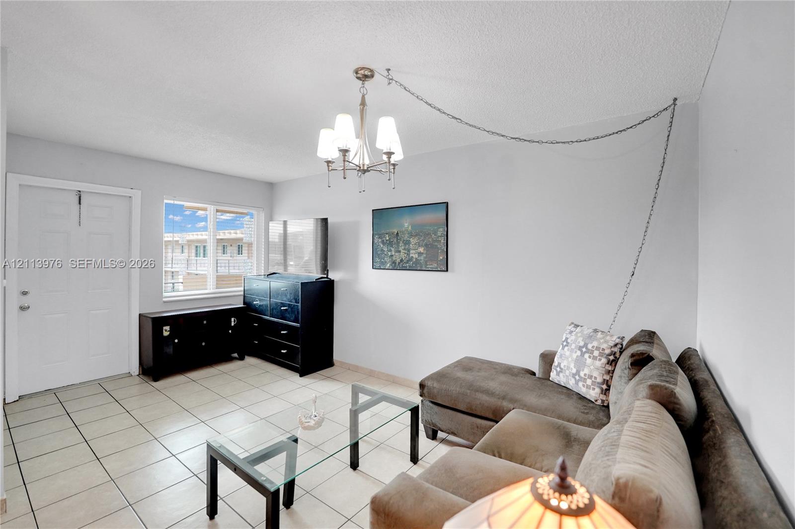 Interior room featuring neutral wall tones, large-format tile flooring, a multi-arm chandelier with chain-link suspension, and a window providing natural light