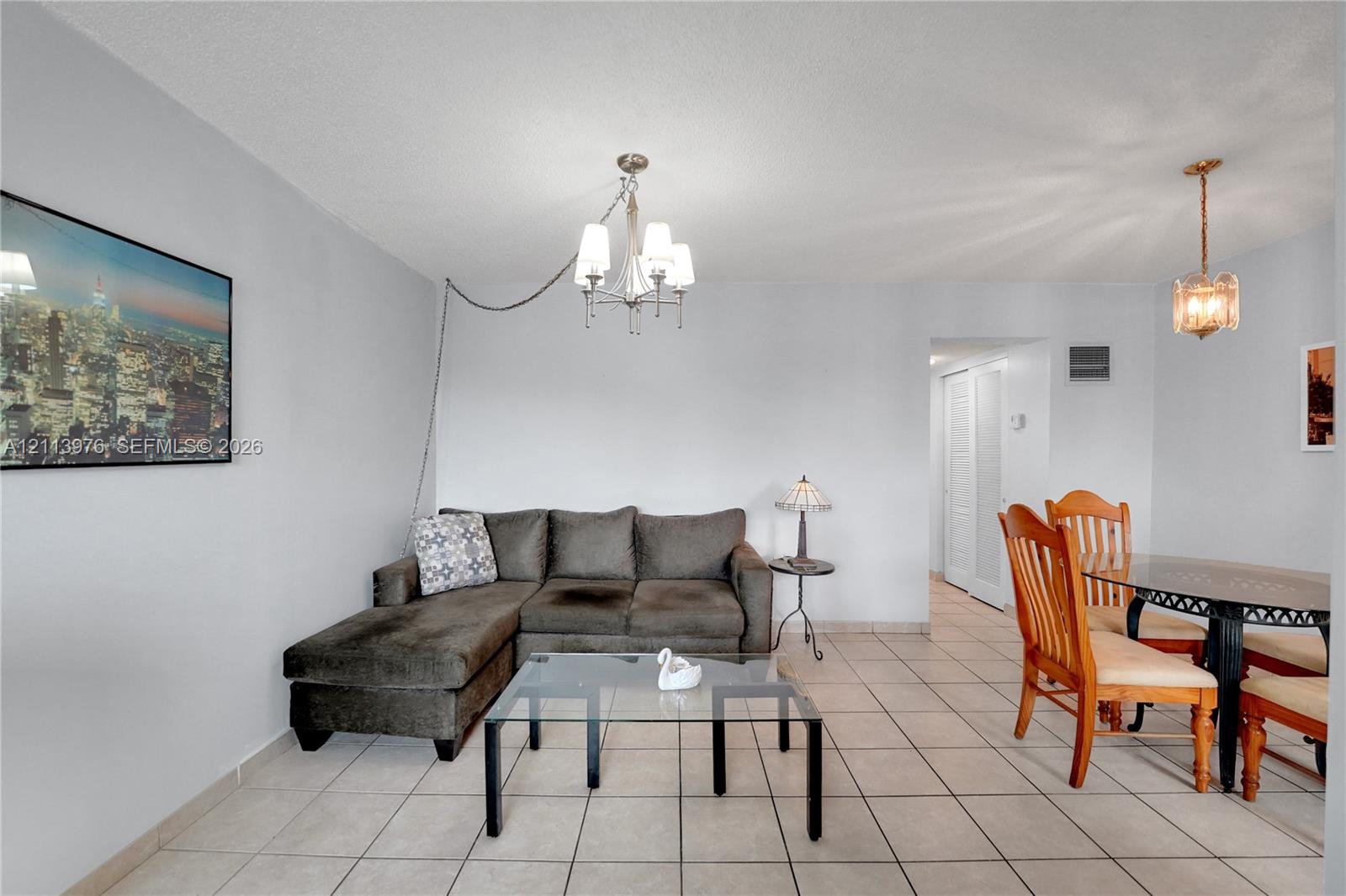 Open-concept area featuring light-toned ceramic tile flooring, a multi-arm metallic chandelier, a decorative pendant light, and double-door closet access
