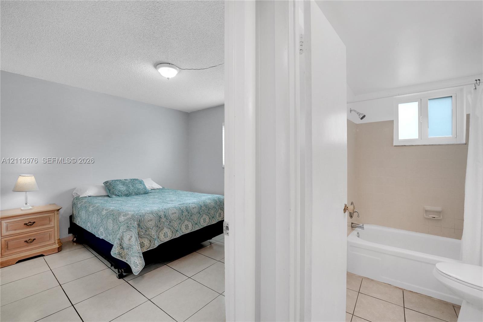 Room featuring large-format ceramic tile flooring and a standard bathtub with a wall-mounted shower fixture and tile surround