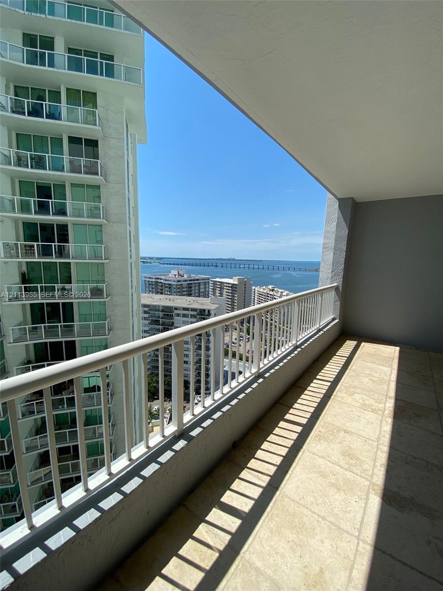 Covered balcony featuring natural stone tile flooring and white metal railings