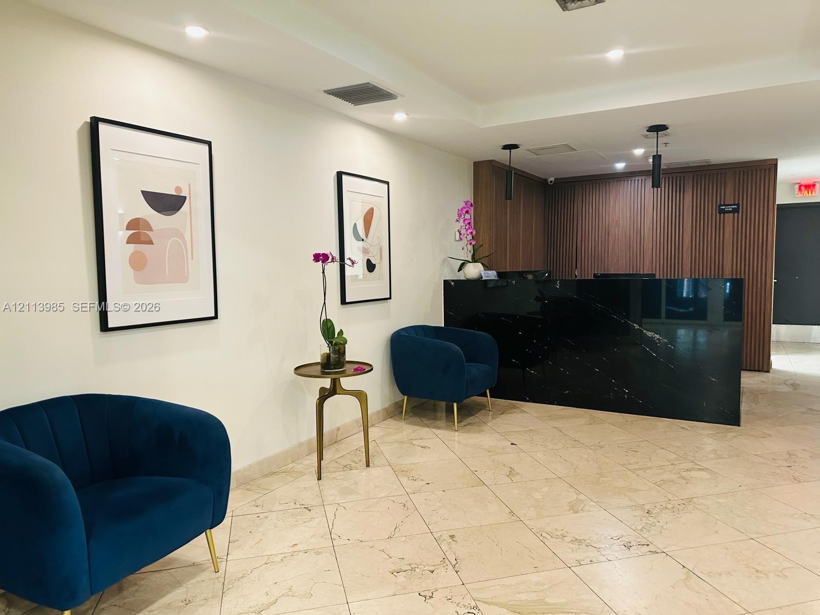 Lobby area featuring large-format stone flooring, a desk with a dark, polished stone front, vertical wood-slat wall paneling, and recessed ceiling lighting