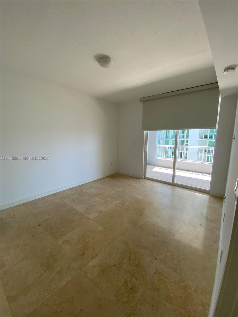 Neutral-toned natural stone flooring, sliding glass balcony door, and roller shade window treatment