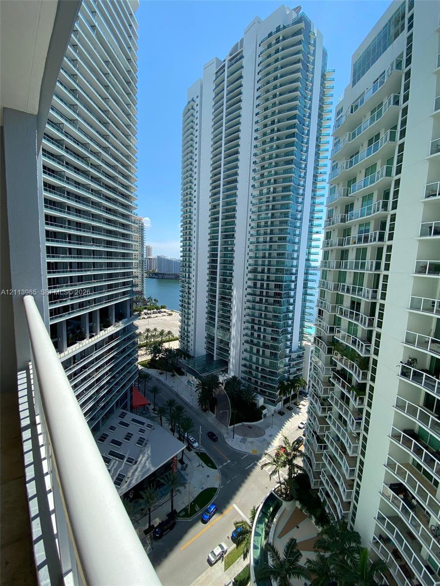 Elevated balcony featuring a glass-panel railing, overlooking a high-rise urban landscape and waterfront scenery
