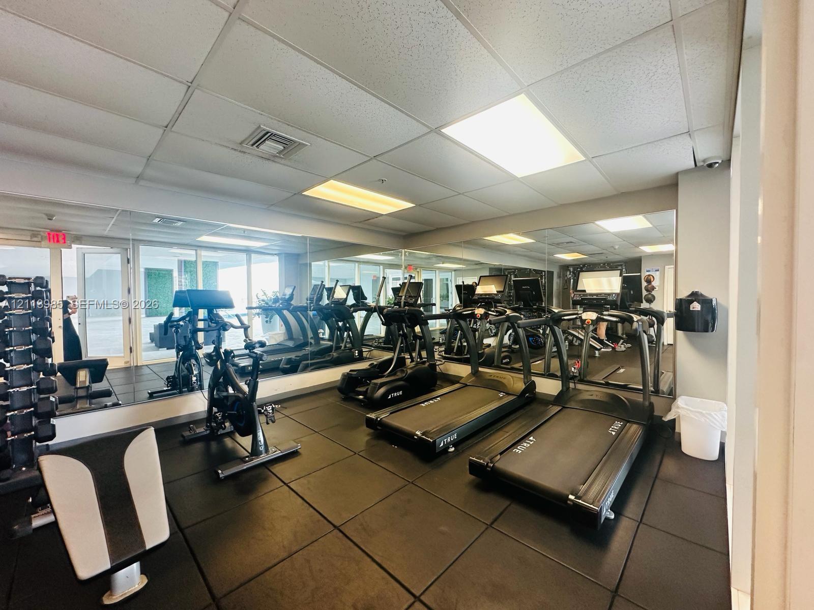 Fitness center featuring rubber flooring, floor-to-ceiling mirrored walls, and recessed lighting