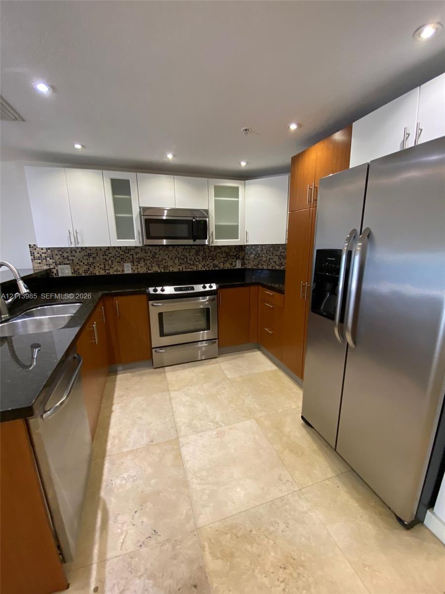 Kitchen featuring two-tone cabinetry, stainless steel appliances, dark stone countertops, mosaic tile backsplash, and light-toned tile flooring