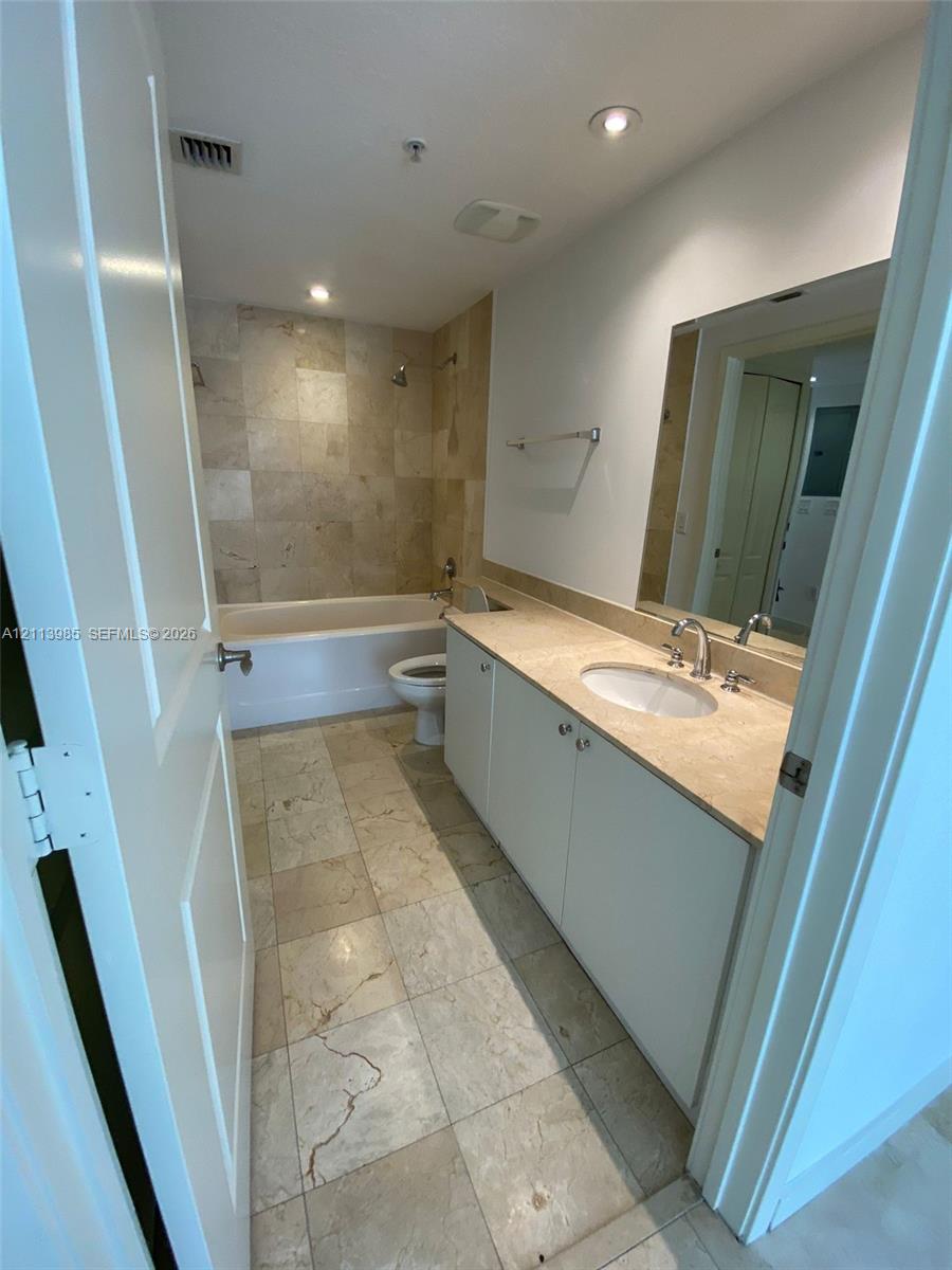 Bathroom featuring large-format tile flooring, tile surround bathtub, white cabinetry, integrated countertop with oval sink, and a wall-mounted mirror