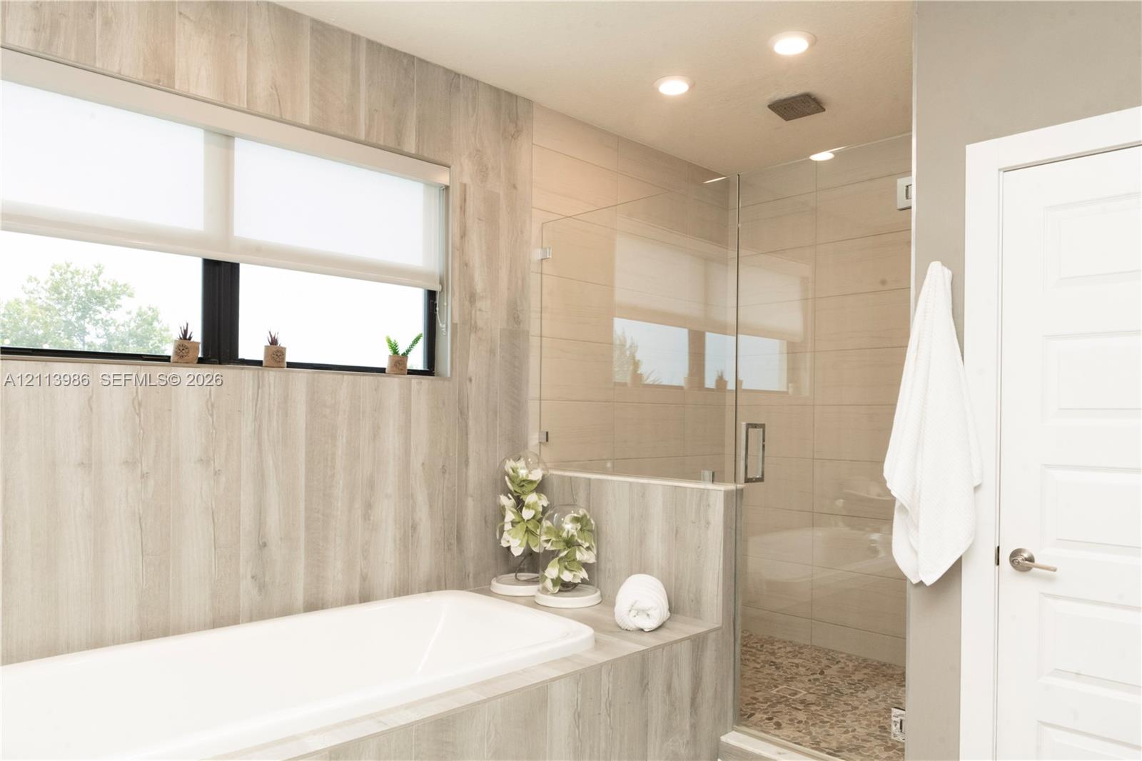 Master bath with frameless glass shower enclosure with pebble stone flooring, and recessed lighting