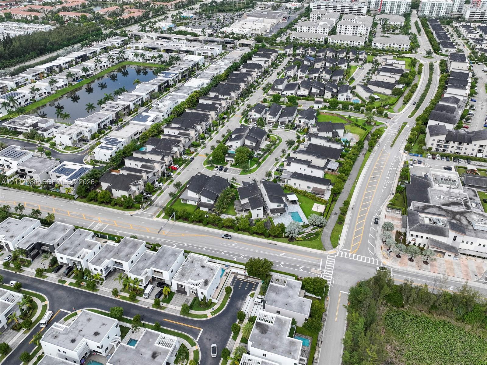 Aerial perspective of a suburban residential community featuring paved thoroughfares, organized residential lots with multi-level dwellings, and a central water feature