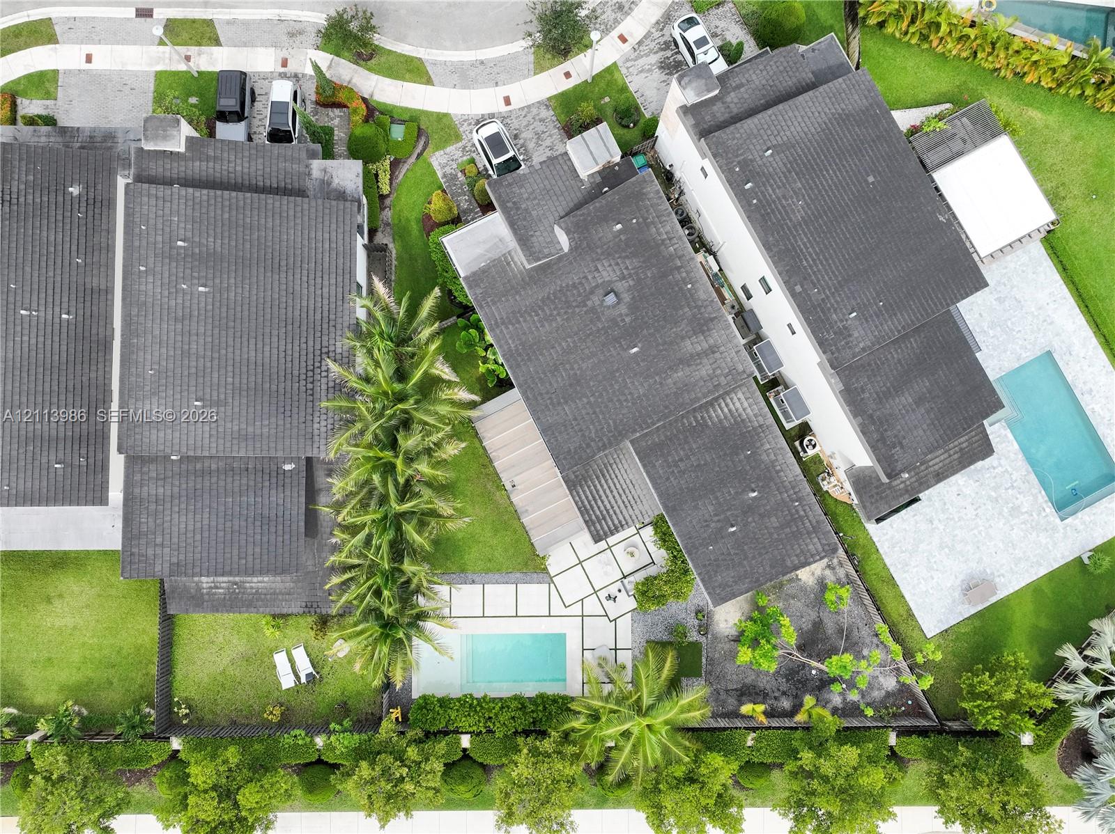Aerial perspective of a multi-story residence featuring a rectangular swimming pool, integrated hardscaped patio, manicured lawn, and mature perimeter landscaping