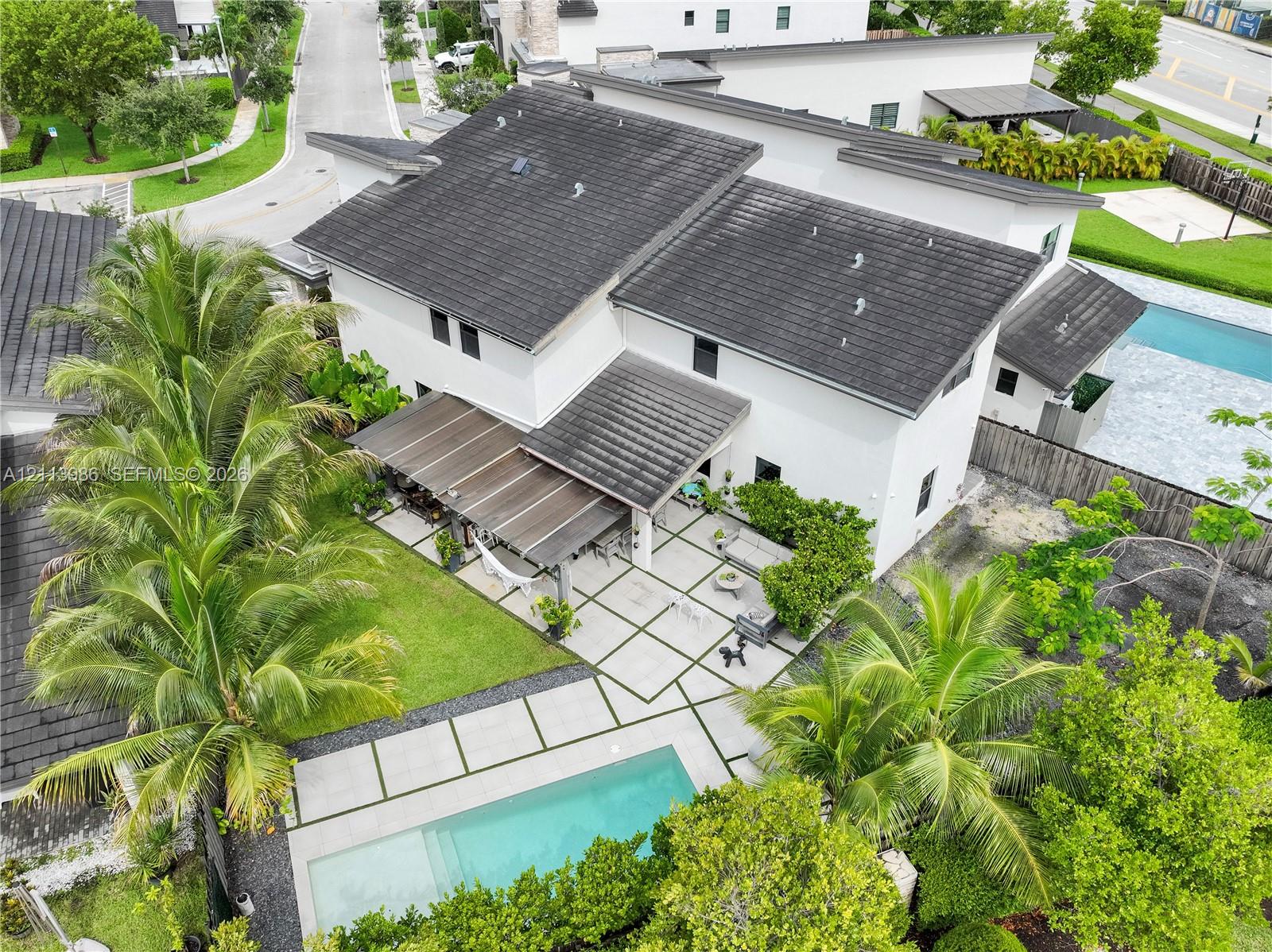 Modern two-story residence featuring a tile roof, an expansive paved patio, a rectangular swimming pool, and mature palm trees Modern two-story residence featuring a tile roof, an expansive paved patio, a rectangular swimming pool, and mature palm trees