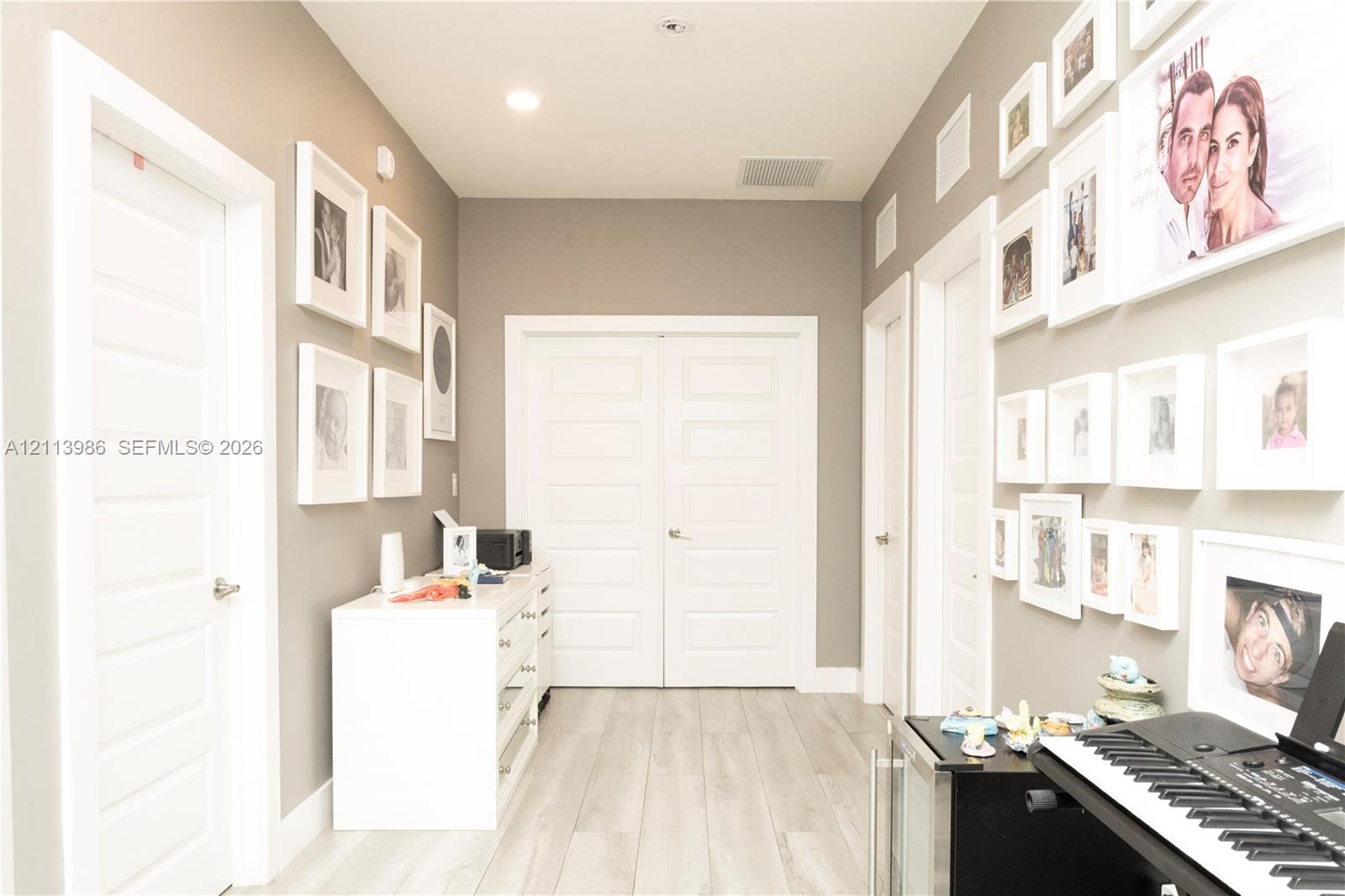Hallway featuring light-toned wood-finish flooring, neutral wall paint, recessed lighting, and multiple white multi-panel doors