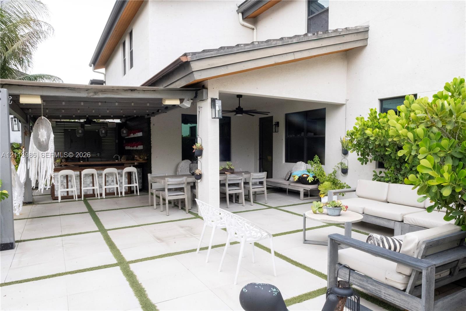 Covered patio featuring a built-in outdoor bar, large-format paver hardscaping with turf infill, a ceiling fan, and exterior wall-mounted lighting Covered patio featuring a built-in outdoor bar, large-format paver hardscaping with turf infill, a ceiling fan, and exterior wall-mounted lighting