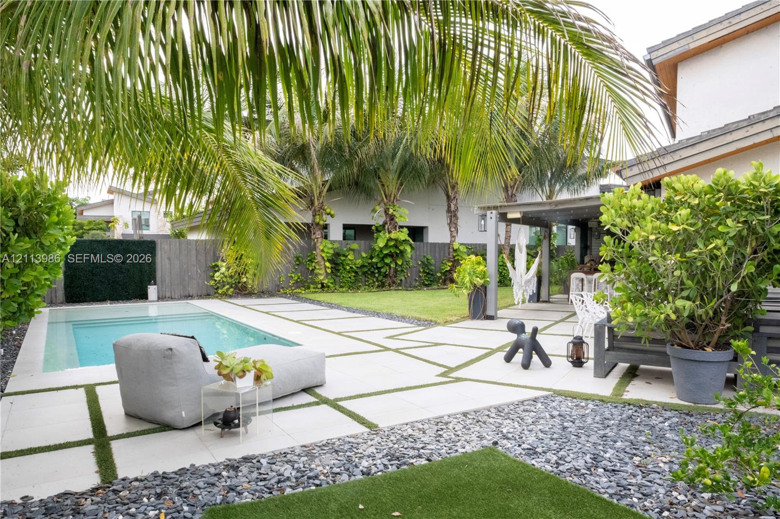 Outdoor living space featuring an in-ground swimming pool, large format concrete pavers with artificial turf inlay, covered patio area, and perimeter landscaping Outdoor living space featuring an in-ground swimming pool, large format concrete pavers with artificial turf inlay, covered patio area, and perimeter landscaping