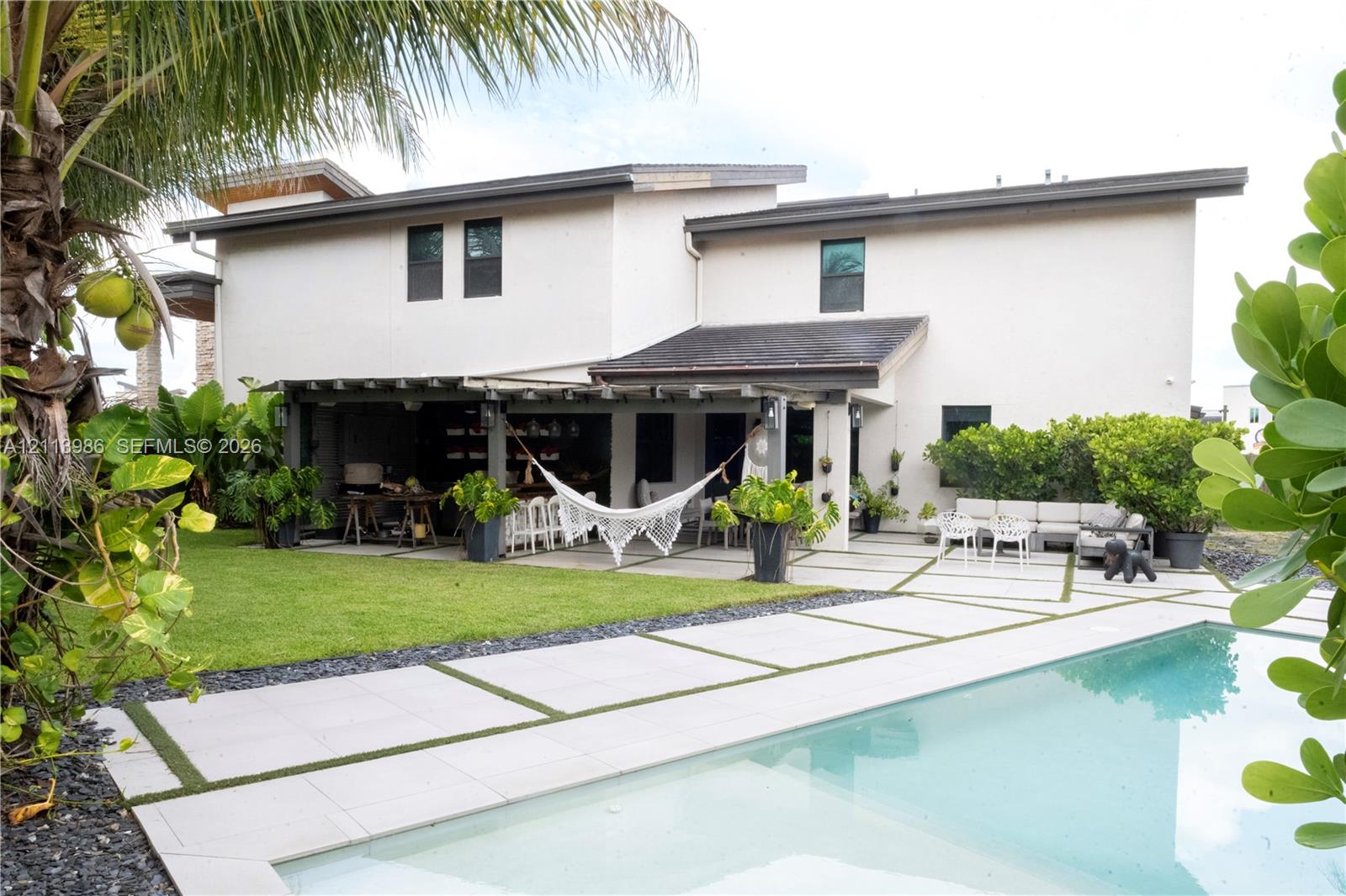Rear exterior featuring a swimming pool with custom concrete paver hardscaping, integrated grass detailing, covered patio, and manicured lawn Rear exterior featuring a swimming pool with custom concrete paver hardscaping, integrated grass detailing, covered patio, and manicured lawn