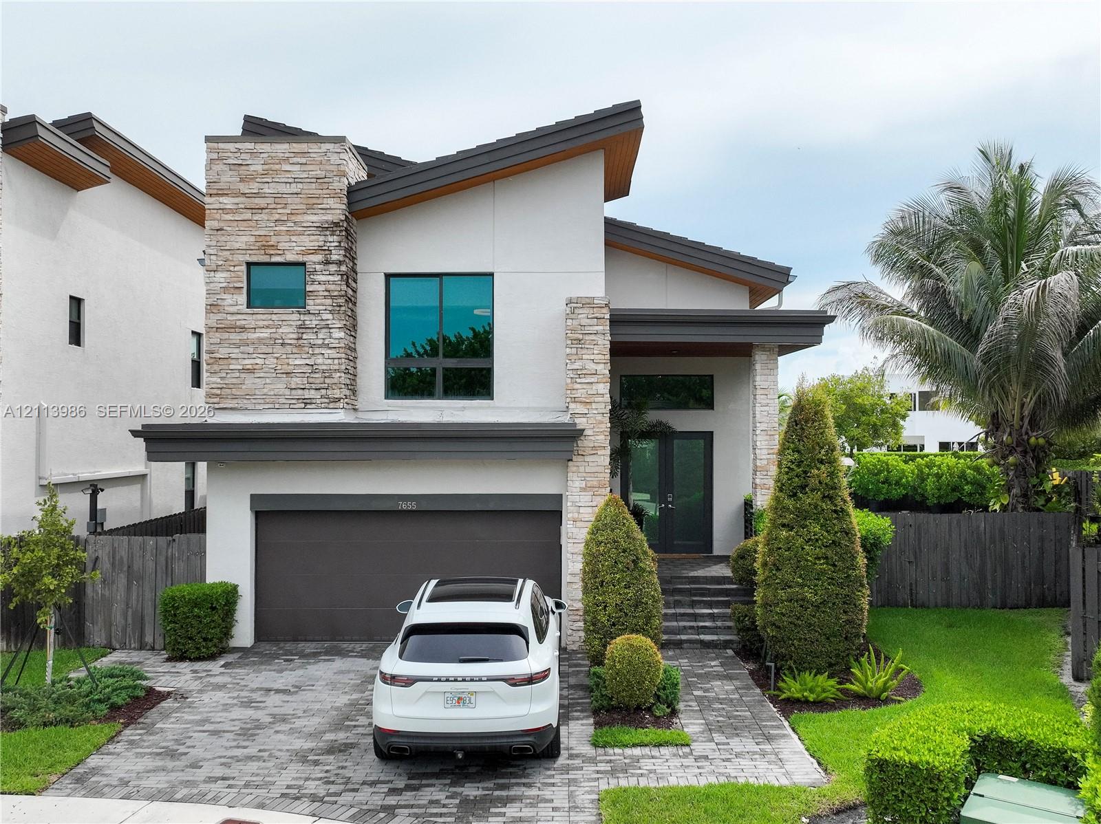Modern exterior featuring stacked stone accents, smooth stucco finish, multi-level roofline, double-door entry, and a paver driveway Modern exterior featuring stacked stone accents, smooth stucco finish, multi-level roofline, double-door entry, and a paver driveway
