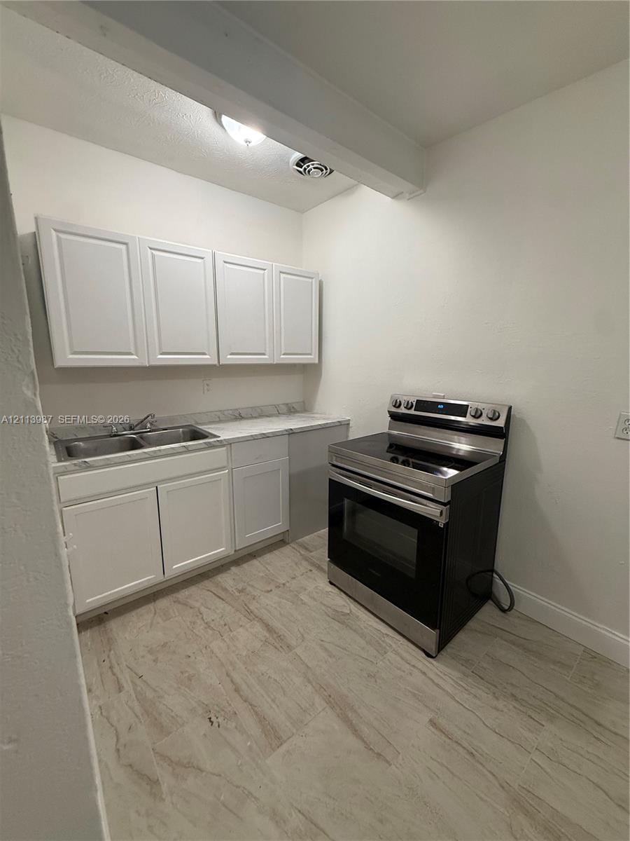 Kitchen featuring white shaker-style cabinetry, stone-patterned countertops, a stainless steel dual-basin sink, a stainless steel electric range, and light-toned tile flooring