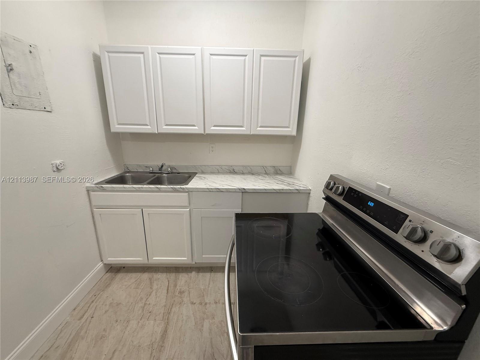 Kitchen featuring white shaker-style cabinetry, stone-patterned laminate countertops, a dual-basin stainless steel sink, wood-finish flooring, and a stainless steel electric range Kitchen featuring white shaker-style cabinetry, stone-patterned laminate countertops, a dual-basin stainless steel sink, wood-finish flooring, and a stainless steel electric range