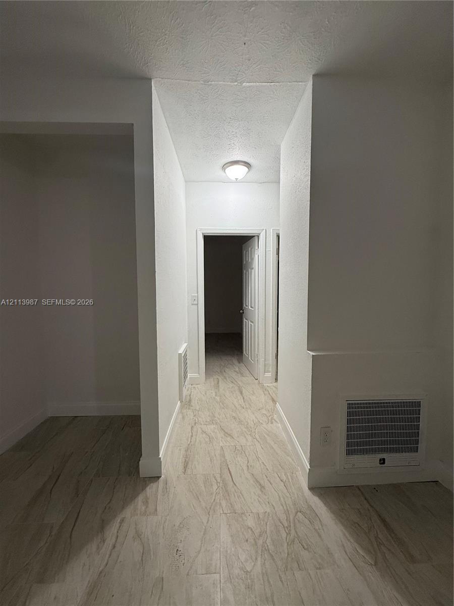 Hallway featuring wood-finish flooring, white walls, and a ceiling-mounted flush light fixture Hallway featuring wood-finish flooring, white walls, and a ceiling-mounted flush light fixture