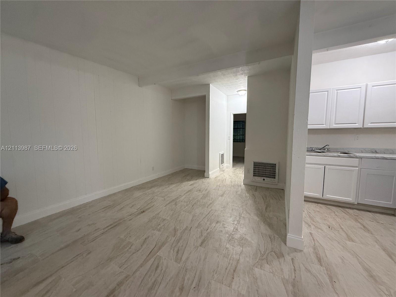 Interior space featuring neutral wall finishes, wood-finish tile flooring, white shaker-style cabinetry, and stone-finish countertops Interior space featuring neutral wall finishes, wood-finish tile flooring, white shaker-style cabinetry, and stone-finish countertops