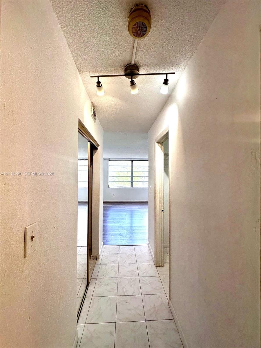 Hallway featuring light-toned tile flooring, a three-bulb adjustable track light fixture, and floor-to-ceiling mirrored closet doors
