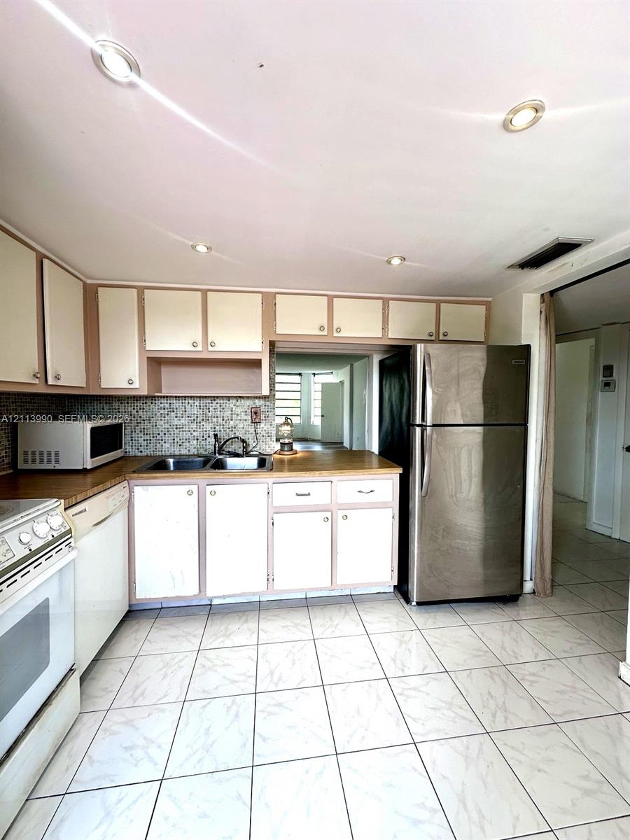 Kitchen featuring solid-surface countertops, mosaic tile backsplash, stainless steel refrigerator, recessed lighting, and tile flooring