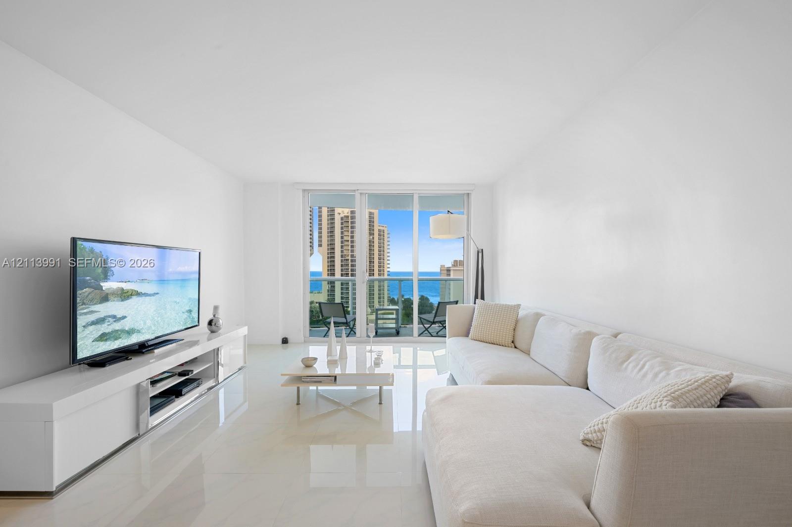 Living area featuring polished stone flooring, floor-to-ceiling glass sliding doors, and a glass-paneled balcony