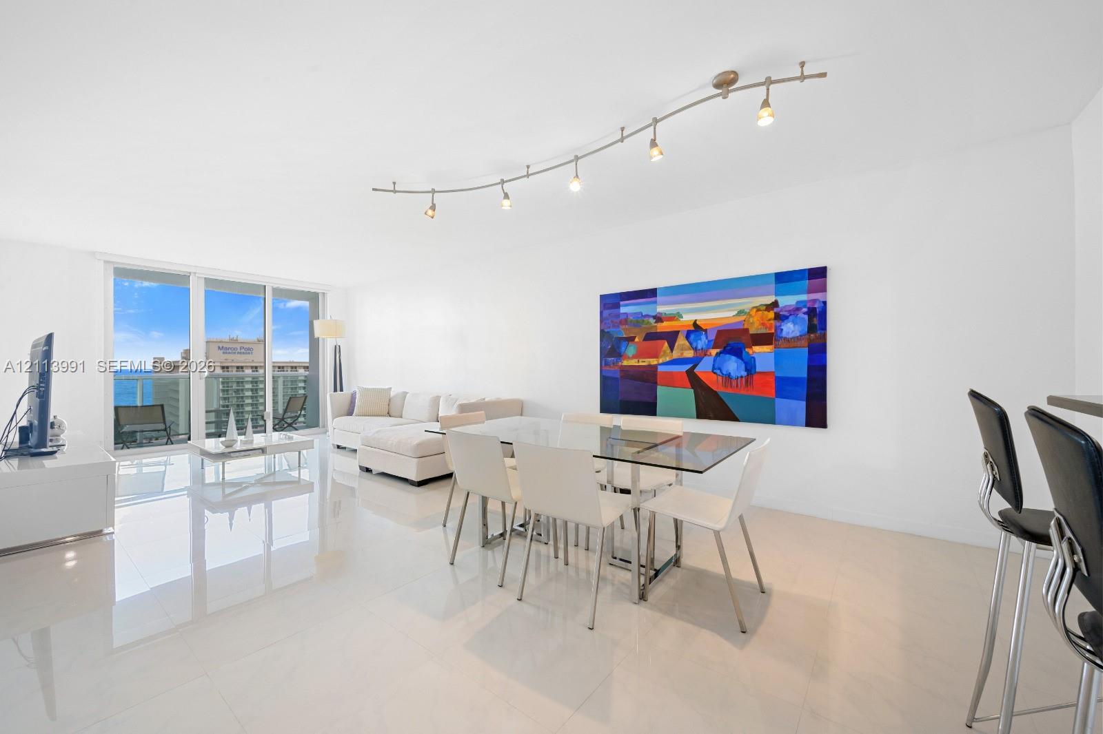 Open-concept room featuring light-toned tile flooring, recessed curved track lighting, and floor-to-ceiling glass sliding doors
