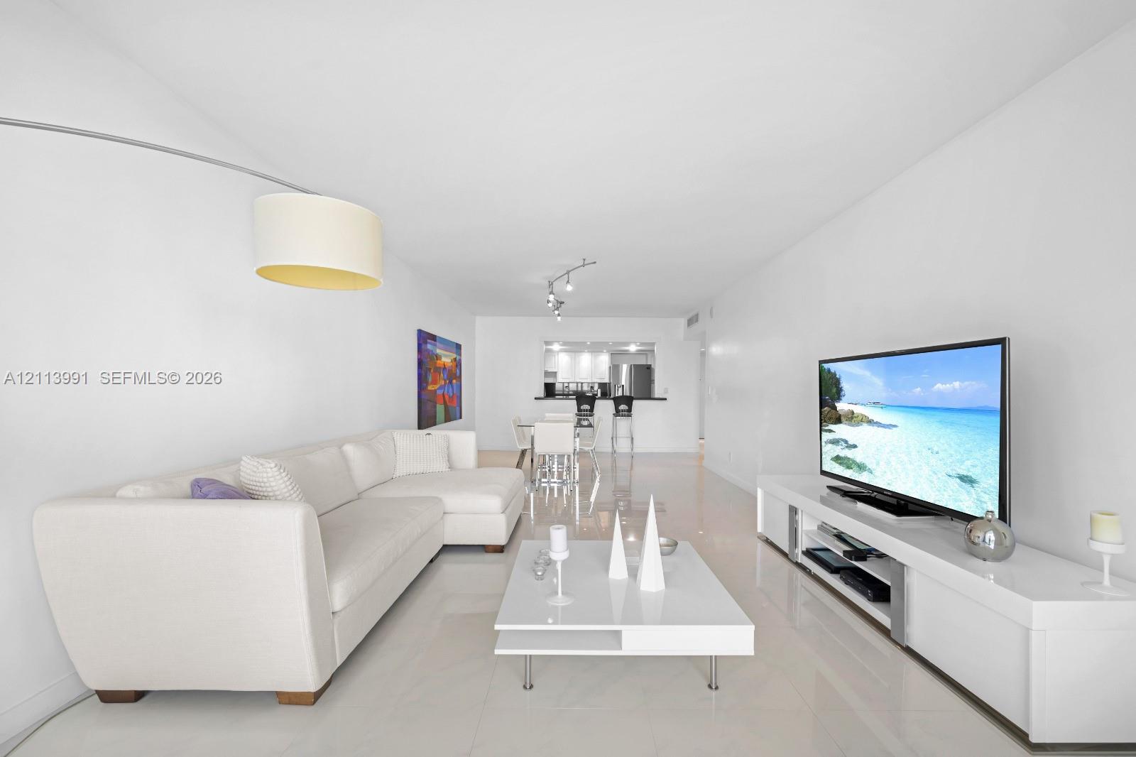Open-concept interior featuring light-toned tile flooring, recessed track lighting, and a breakfast bar pass-through