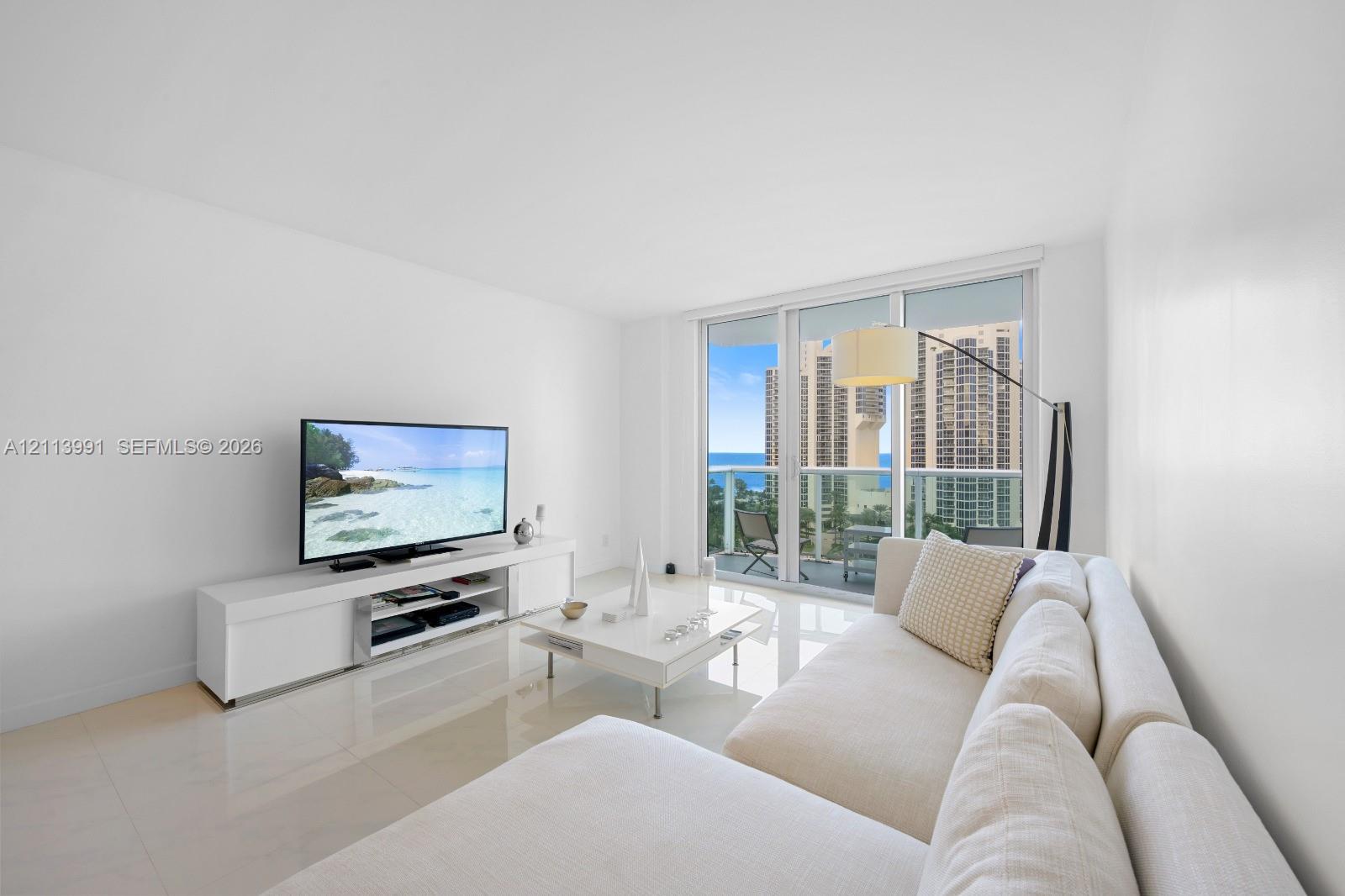 Living area featuring polished tile flooring, floor-to-ceiling glass sliding doors, and a private balcony with ocean and city scenery