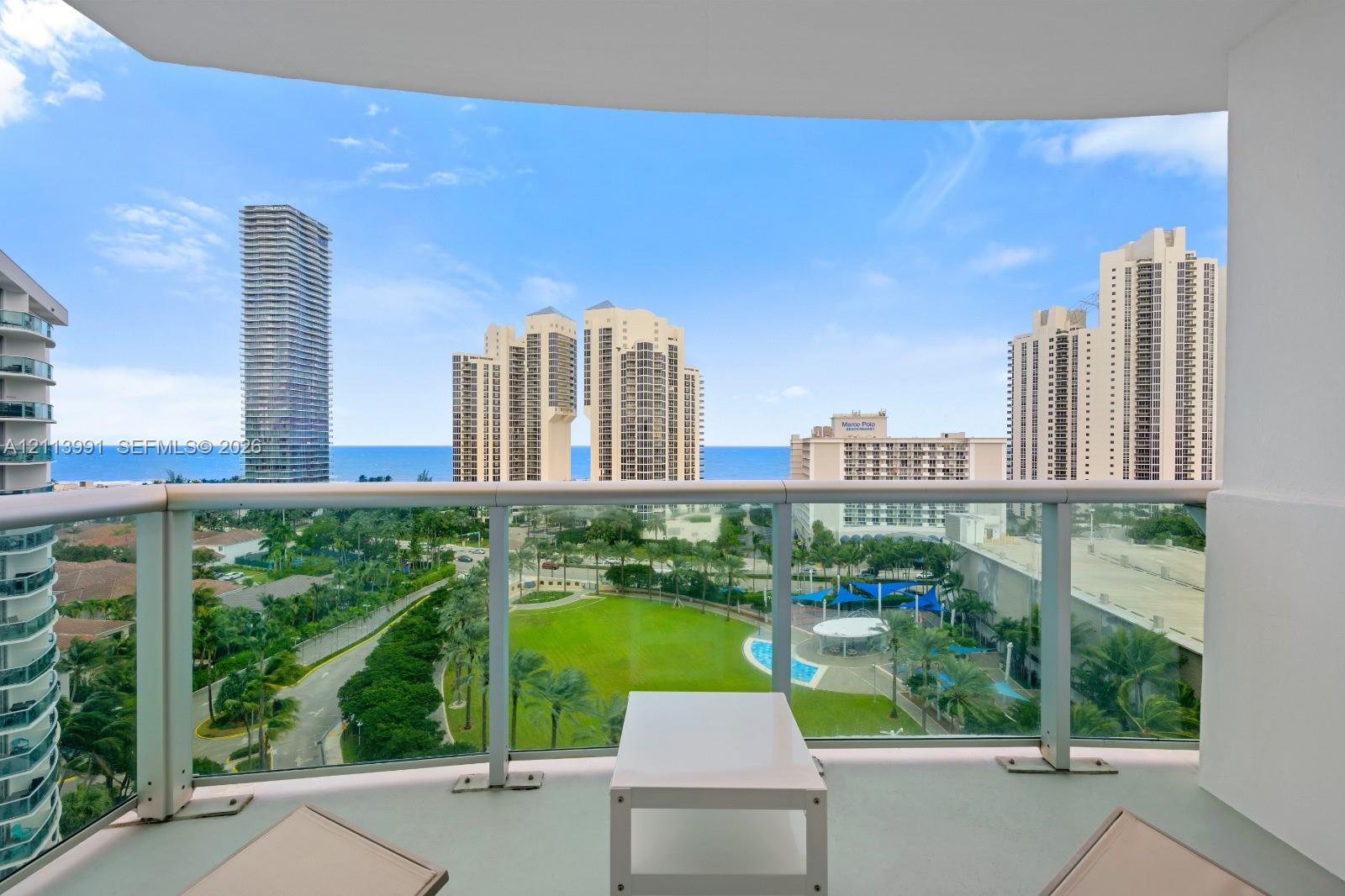 Covered balcony with glass and metal railings, concrete flooring, and panoramic ocean and urban skyline scenery