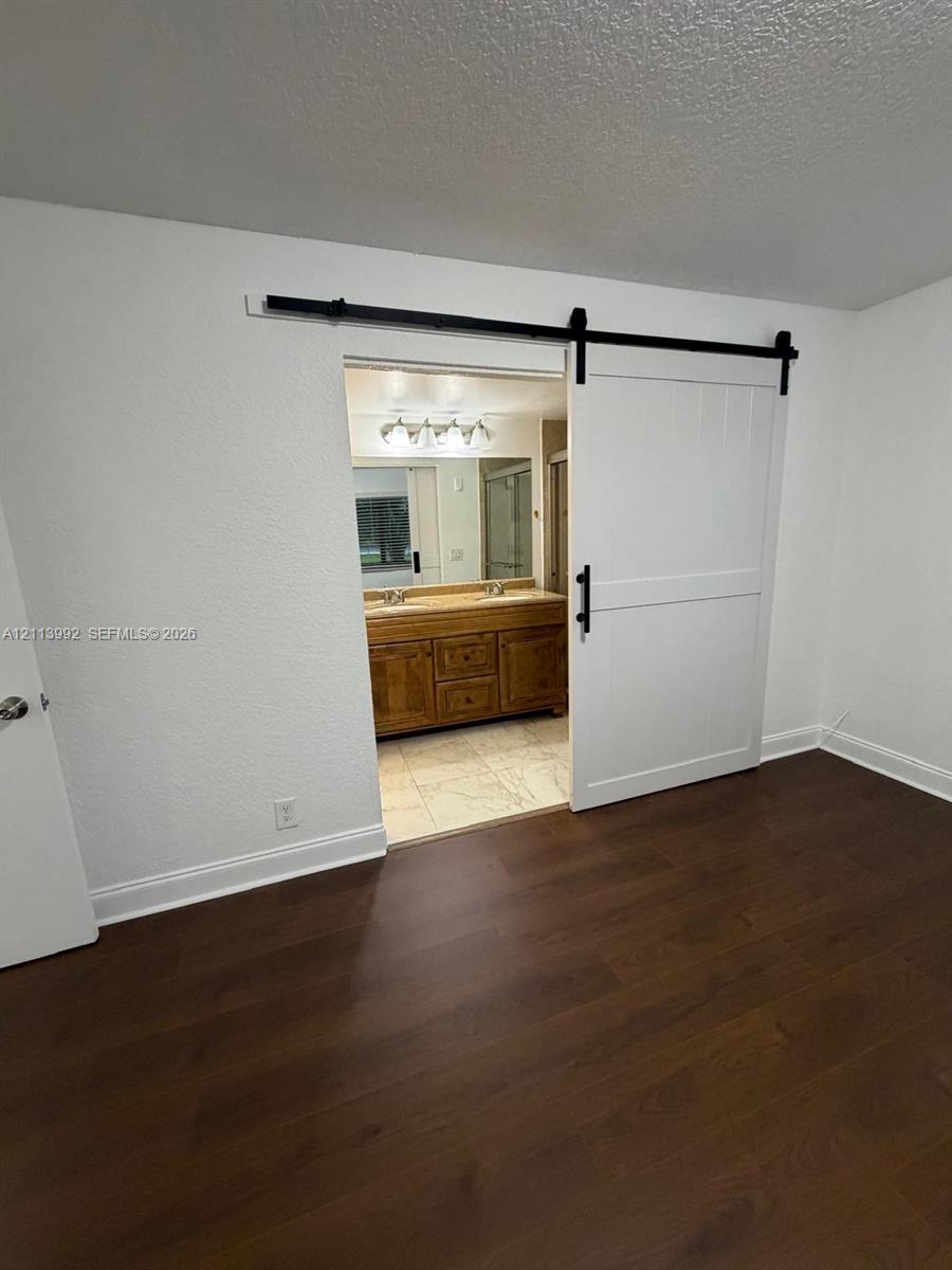 Wood-finish flooring featuring a white sliding barn door on a black metal track, with an attached bathroom vanity including dual sinks, cabinet storage, and four-light vanity fixture