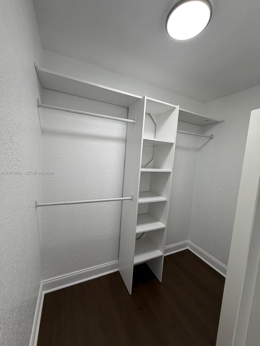 Walk-in closet featuring white built-in shelving, dual-tier hanging rods, dark wood-finish flooring, and a flush-mount ceiling fixture