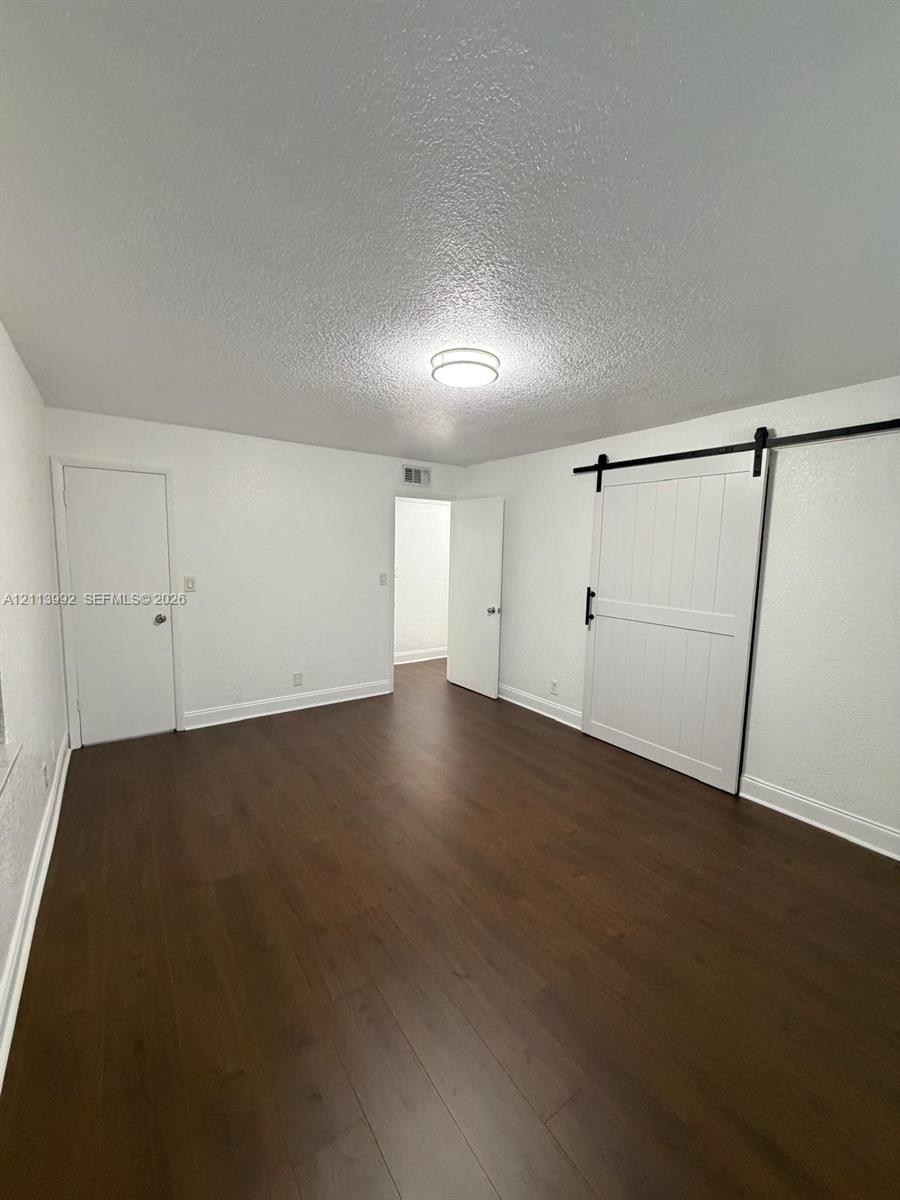 Interior space featuring wood-finish flooring, white walls, flush-mount ceiling lighting, and a white sliding barn-style door with matte black hardware