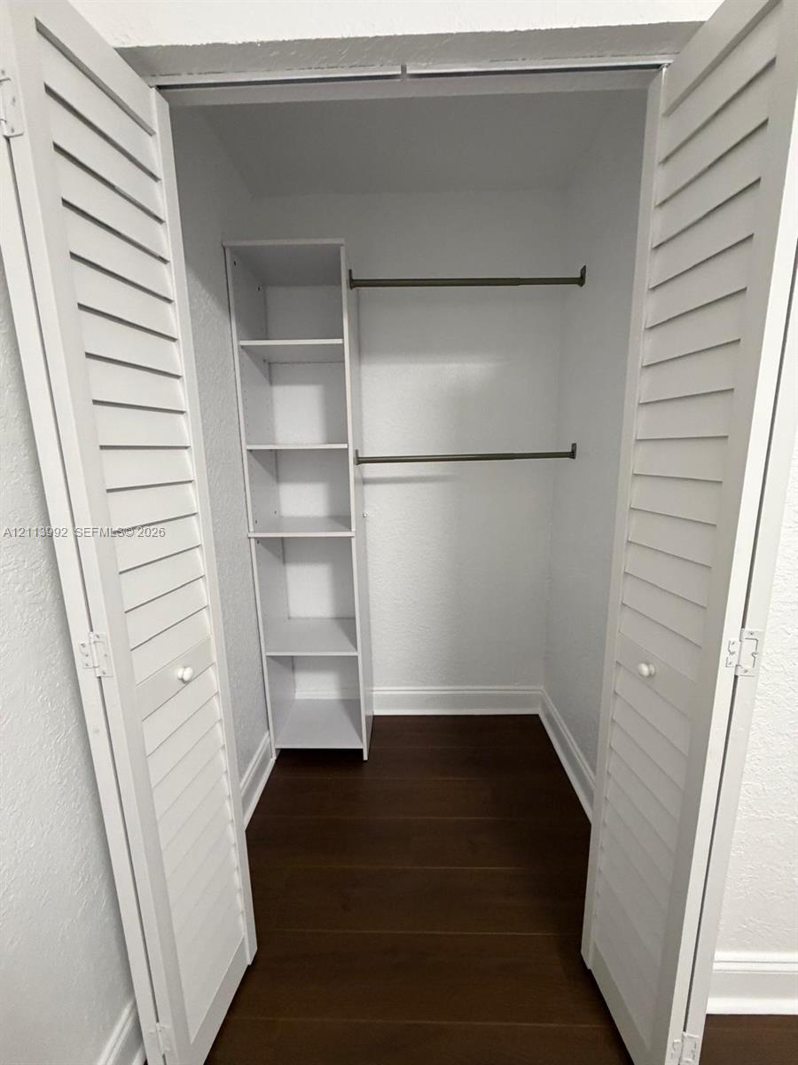Closet featuring white louvered bifold doors, wood-finish flooring, built-in shelving, and dual metal clothing rods