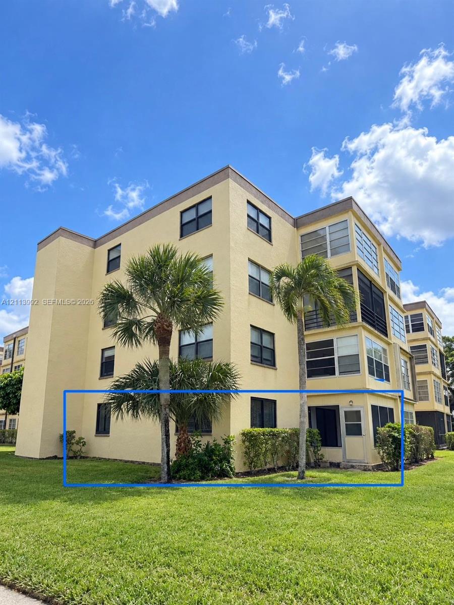 Stucco exterior multi-story building featuring ground-level screened-in patio, lush landscaping, and mature palm trees