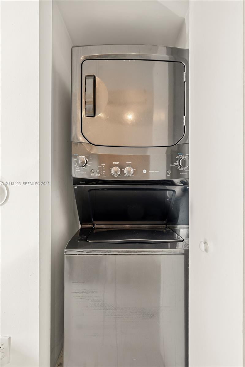 Stacked metallic laundry unit featuring a top-mounted dryer and front-loading washing machine housed within a dedicated enclosure