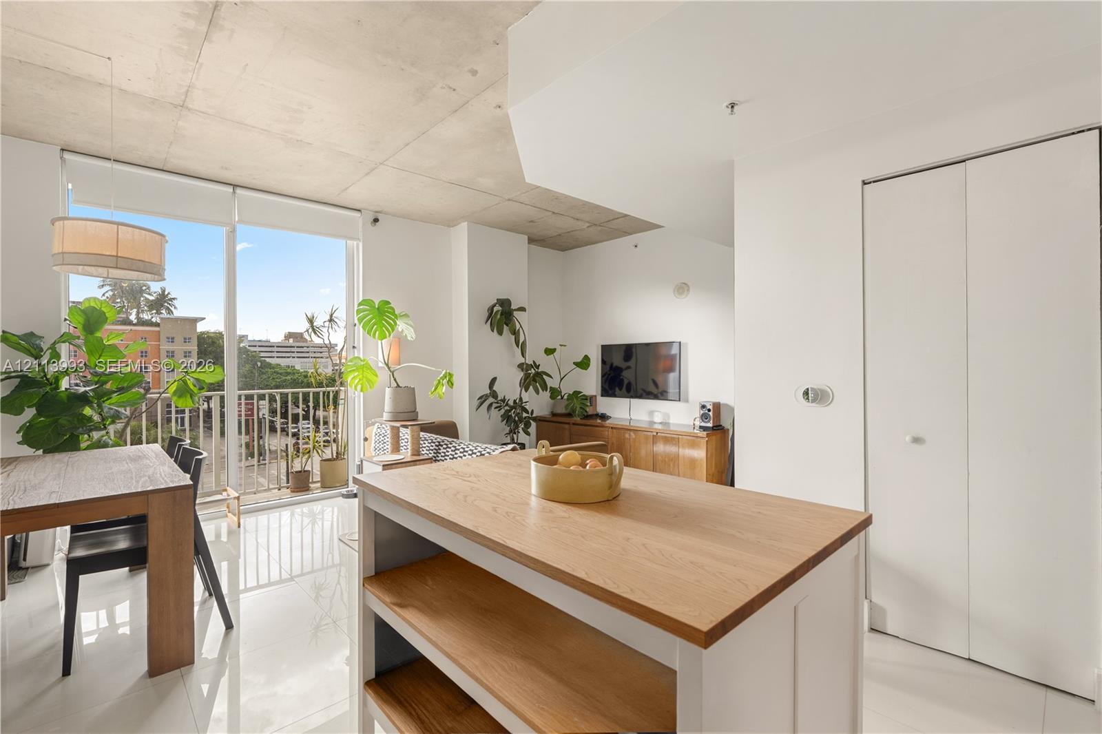Exposed concrete ceiling, floor-to-ceiling glass door, private balcony, wood-top kitchen island, and polished floor tile