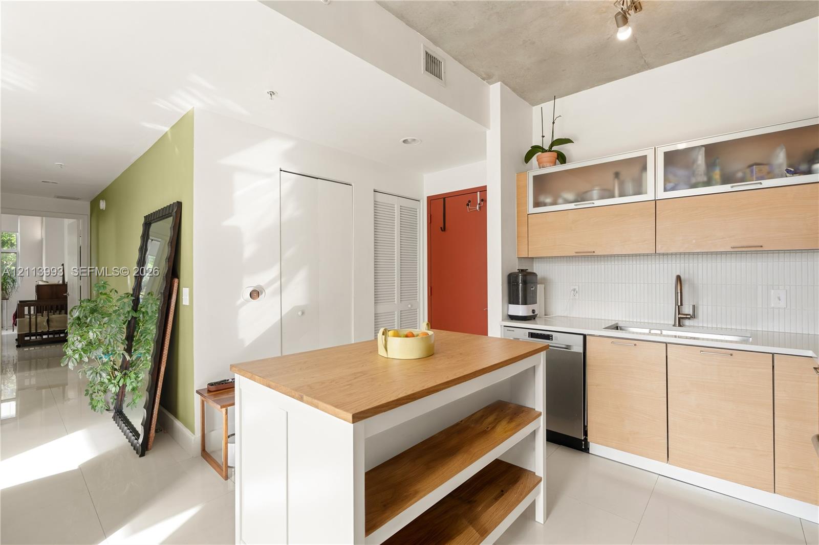 Kitchen featuring light wood-finish cabinetry, white solid-surface countertops, industrial-style exposed concrete ceiling, tiled backsplash, and a white kitchen island with open wood shelving